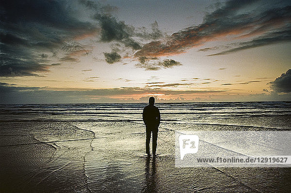 A man stands on the beach watching the waves and sunset over the Pacific Ocean  Oregon  USA