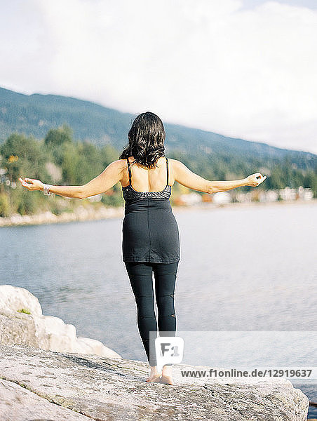 Rear view of woman with black hair and arms outstretched doing yoga on seashore