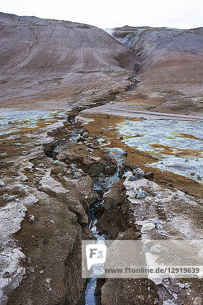 A cobalt coloured stream flows down from Namafjall mountain through the Hverarˆšˆ‚ndor Hverir Geothermal Area traversing brightly coloured minerals and soil at Namaskard Pass North Iceland.