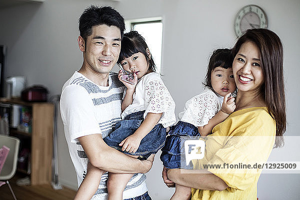 Portrait of Japanese man and woman with two young girls standing in a living room  smiling at camera.