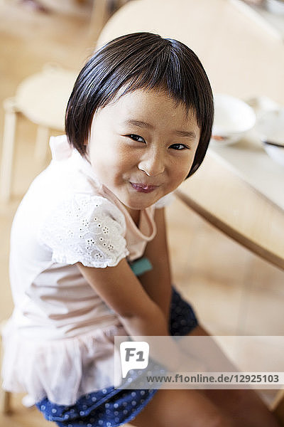 Ein lächelndes Mädchen sitzt in einer japanischen Vorschule auf dem Boden und schaut in die Kamera.