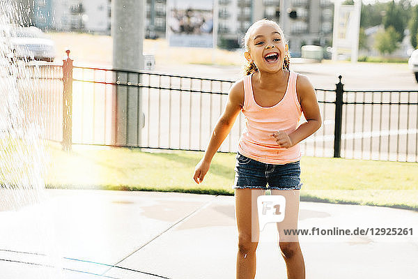 Lächelndes Mädchen spielt im Sommer im öffentlichen Brunnen