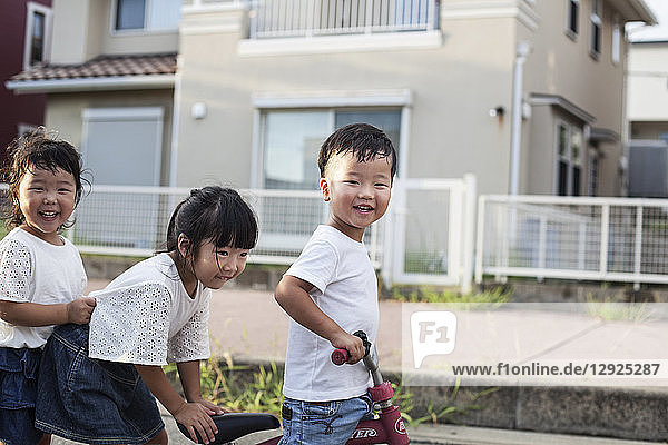 Portrait of two Japanese girls and boy playing on street with a bicycle  smiling at camera.