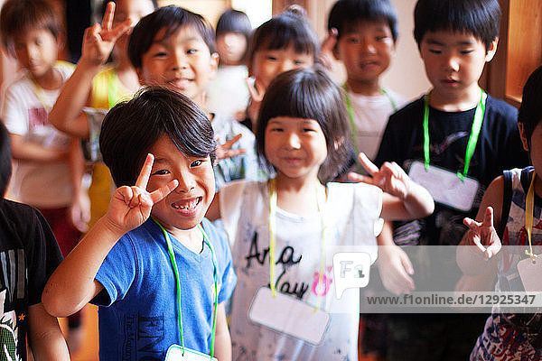 Group of smiling children in a Japanese preschool  making peace sign  looking at camera.