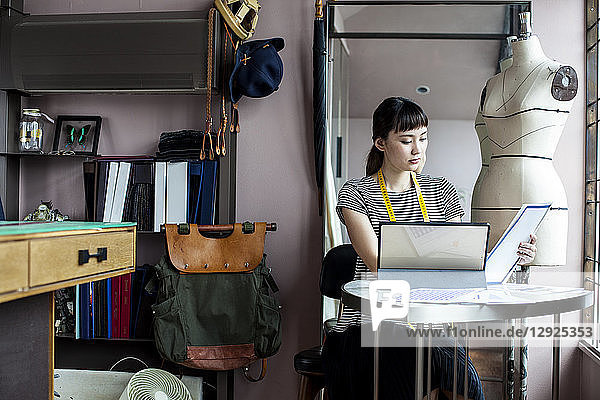 Japanese female fashion designer working in her studio  sitting at table  looking at fabric samples.