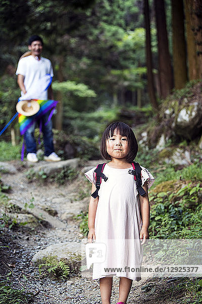 Japanese girl wearing pale pink sun dress and carrying backpack standing in a forest  man in the background.