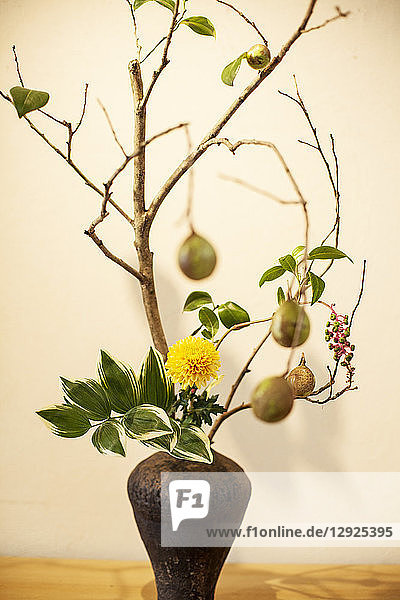 Nahaufnahme des Ikebana-Arrangements mit Zweigen  Blättern  Früchten  Beeren und gelber Blüte in brauner Vase.