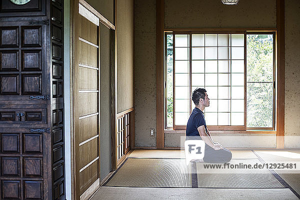 Japanischer Mann kniend auf Tatami-Matte in traditionellem japanischen Haus.