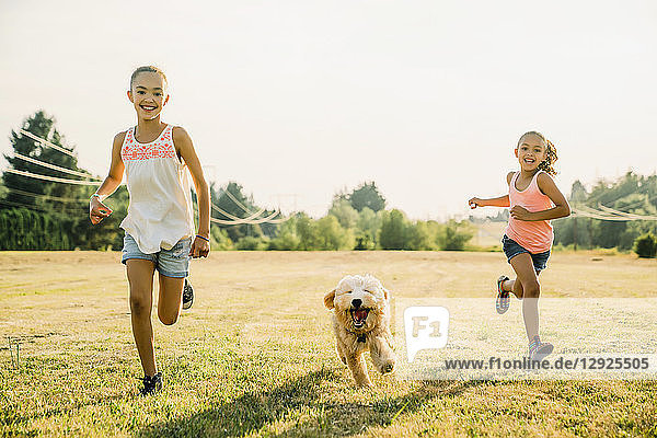 Mädchen rennen mit Labradoodle-Welpe durchs Feld