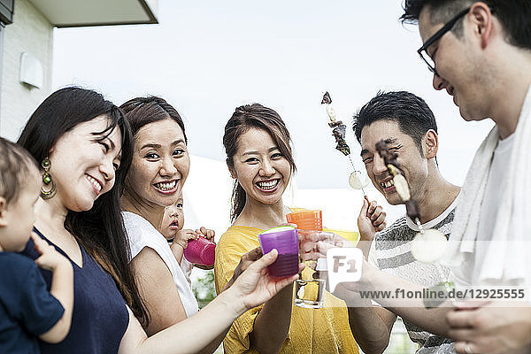Gruppe fröhlicher junger japanischer Männer und Frauen  die im Freien stehen und mit Plastikbechern anstoßen.