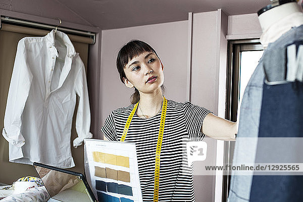 Japanische Modedesignerin  die in ihrem Atelier arbeitet und ein Kleidungsstück auf einem Schneiderinnenmodell betrachtet.