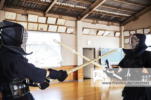 Zwei japanische Kendo-Kämpfer mit Kendo-Masken beim Üben mit dem Holzschwert in der Turnhalle.