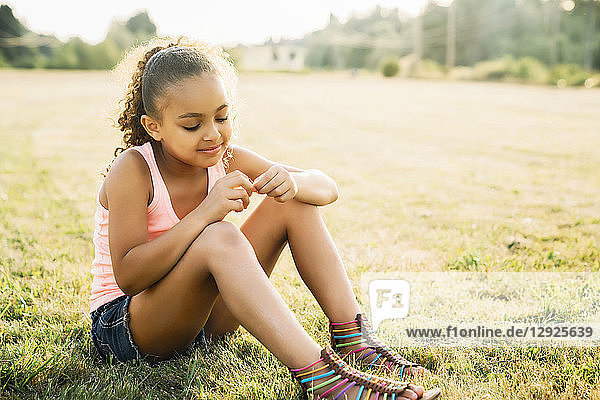 Girl sitting in field looking at flower in her fingers