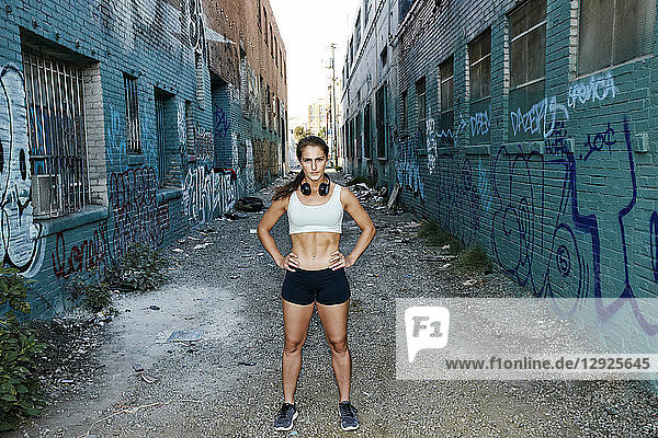 Weibliche Sportlerin steht auf einer Straße  die von mit Graffiti beschmierten Gebäuden gesäumt ist.