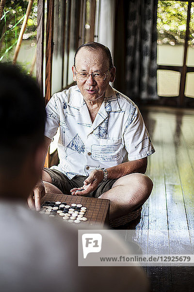 Zwei japanische Männer sitzen auf dem Boden auf der Veranda eines traditionellen japanischen Hauses und spielen Go.