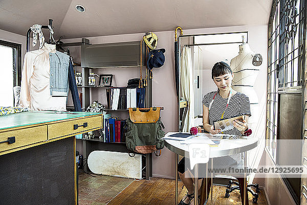 Japanese female fashion designer sitting at desk  working in her studio.