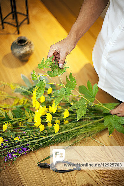 Person in einer Blumengalerie  die an einem Ikebana-Arrangement mit Blättern  gelber und violetter Blume arbeitet.