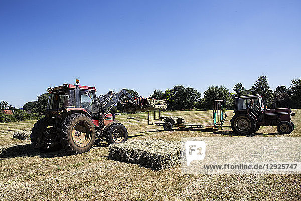 Tractor in a field  loading hay bales onto a trailer.