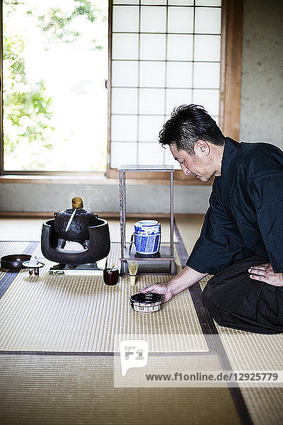 Japanischer Mann in traditionellem Kimono  auf dem Boden kniend  eine Teeschale haltend  während der Teezeremonie.