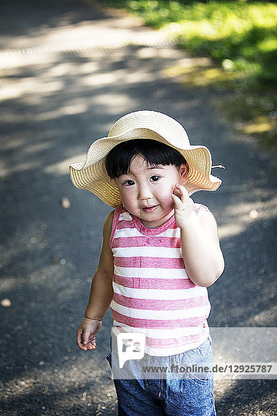 Two Japanese girls wearing sun hats standing on path holding hands.