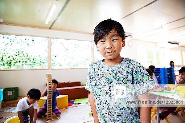 Young boy standing in a classroom in a Japanese preschool  smiling at camera.