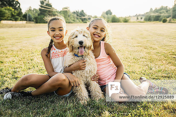 Portrait of smiling happy girls hugging labradoodle puppy in park