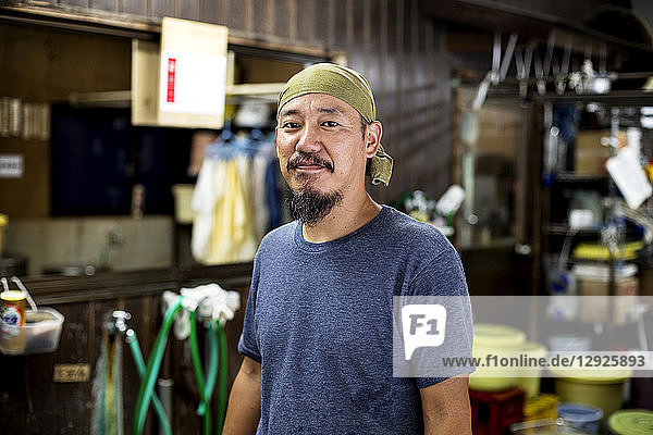 Japanese man wearing bandana in a textile dyeing workshop  smiling at camera.