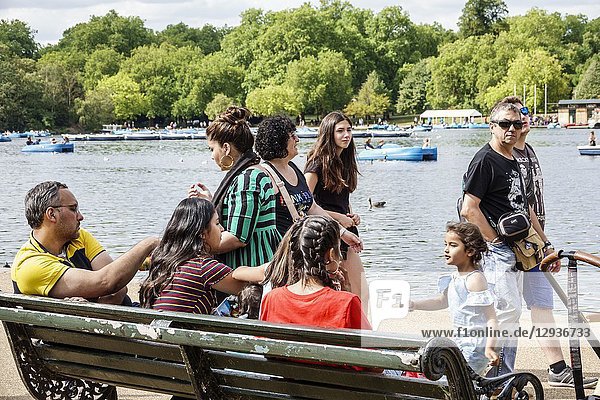 United Kingdom Great Britain England  London  Royal Parks  Hyde Park  green space  The Serpentine  recreational lake  boats  bench  Hispanic  man  woman  girl  teen  child  family  sitting  strolling