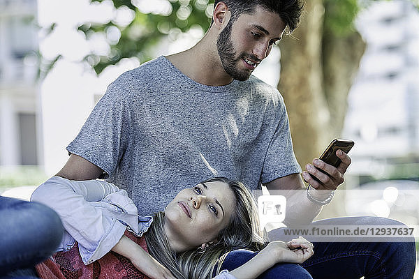 Mann benutzt ein Smartphone,  während sich eine Frau auf seinem Schoß entspannt