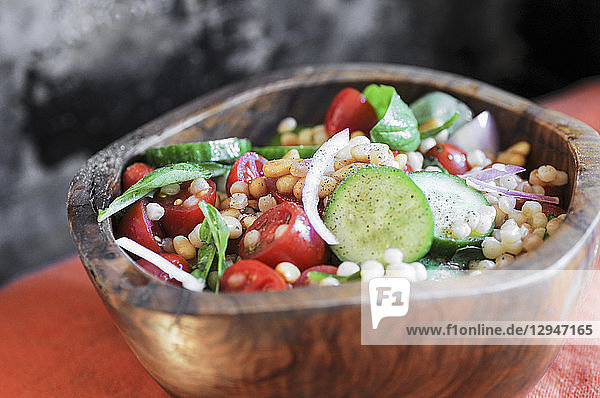 Israelischer Couscoussalat mit Gurken  Tomaten und frischem Basilikum in einer Holzschale
