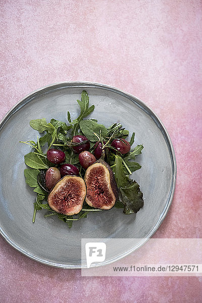 Ein Salat mit Feigen  Trauben und Kopfsalat auf einem grauen Teller vor einem rosa Hintergrund