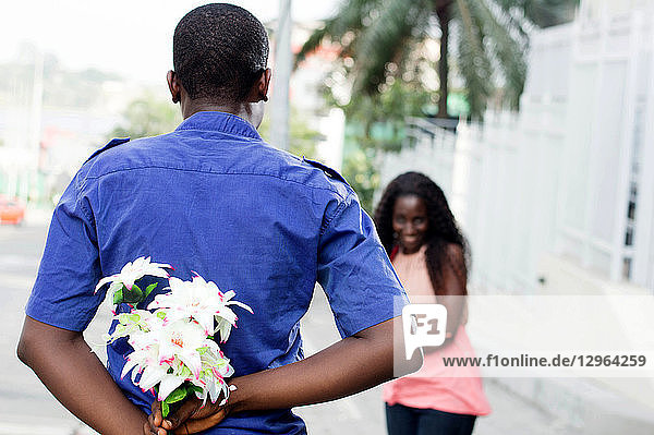 Der junge Mann versteckt eine Blume in seinem Rücken und schenkt sie der jungen Frau zu ihrer Überraschung.