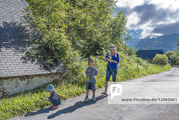 France  Pyrenees National Park  Val d'Azun  Aucun  a woman and her children walking on the road and picking up flowers.