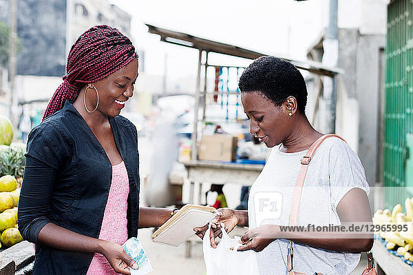 Young happy women at the market looking in a bag containing fruit.