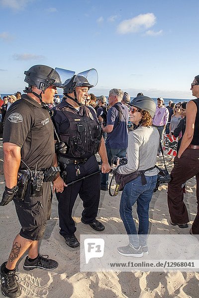 A female newspaper photographer is greeted by police at a political demonstration in Laguna Beach  CA. Note that both are wearing hard hats.