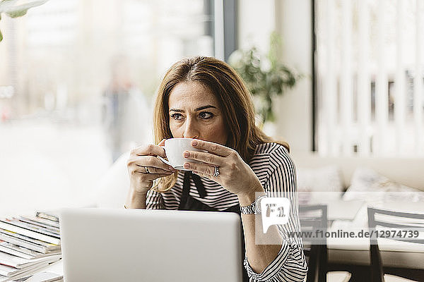 Barista drinking coffee by laptop in cafe