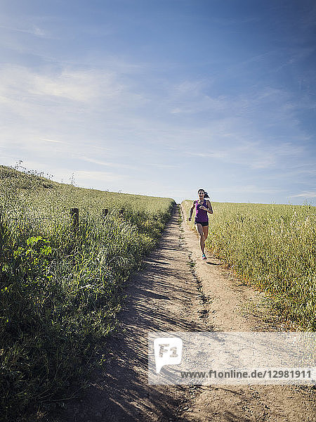 Mittlere erwachsene Frau joggt auf einem Weg durch ein Feld
