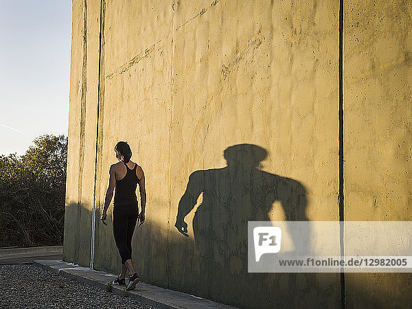 Frau in Sportkleidung geht an einer Betonmauer vorbei