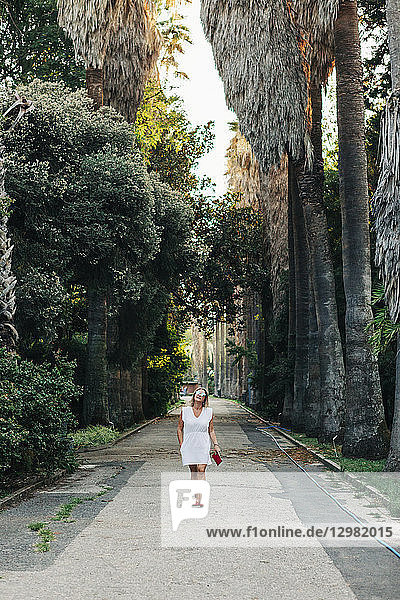 Frau in weißem Kleid geht auf Fußweg zwischen Palmen