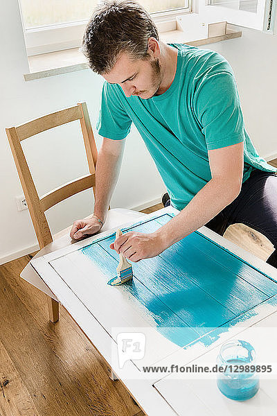 DIY - Mann streicht Holzplatte mit türkiser Farbe