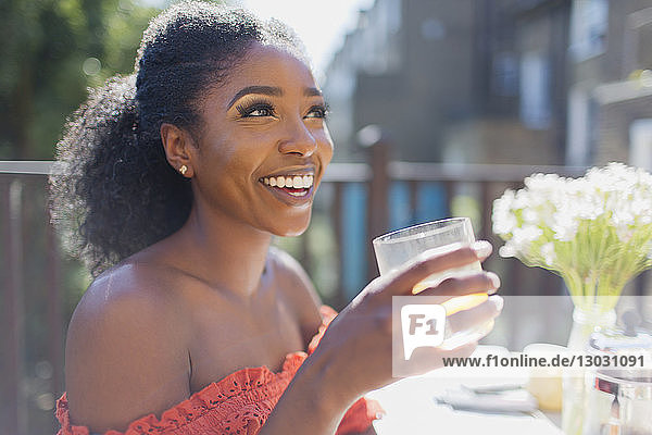 Happy young woman drinking orange juice on sunny balcony