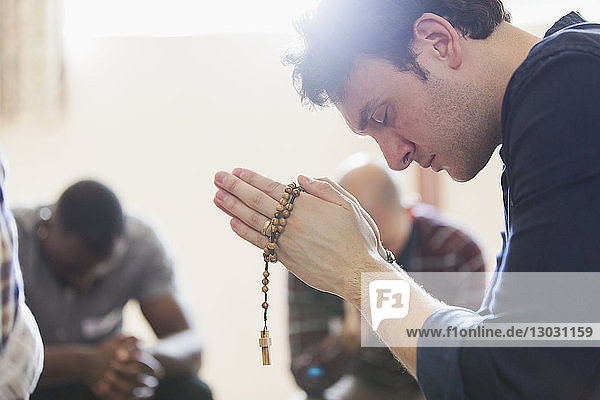 Gelassener Mann betet mit Rosenkranz in Gebetsgruppe