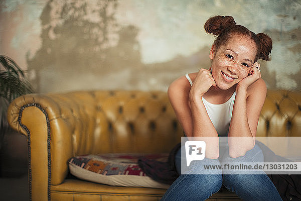 Porträt einer lächelnden  selbstbewussten jungen Frau  die auf einem Sofa sitzt