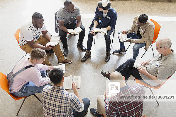 Men reading and discussing bible in prayer group circle