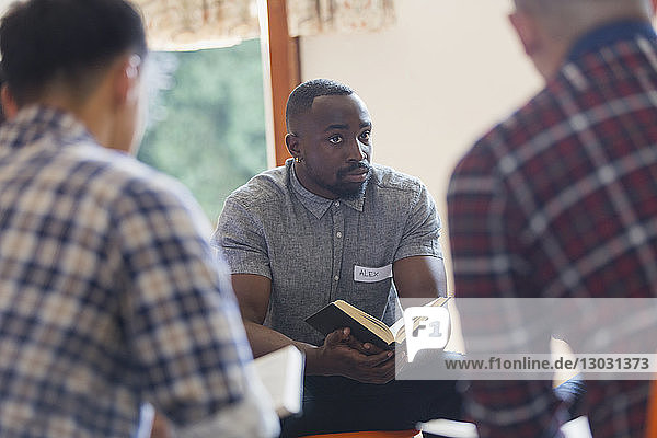 Aufmerksamer junger Mann mit Bibel in Gebetsgruppe