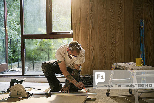 Construction worker measuring wood board in house