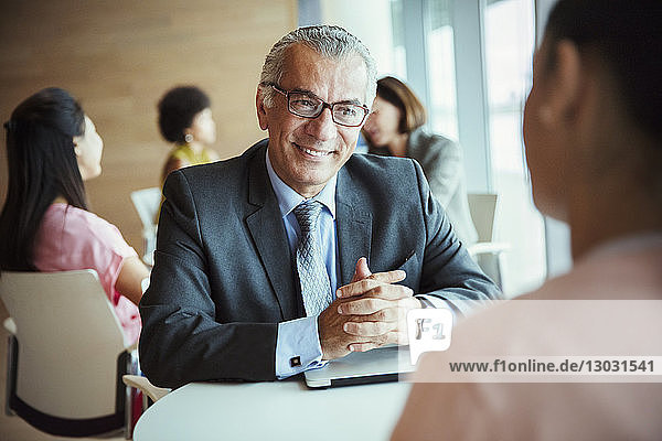 Smiling businessman listening to colleague in cafeteria
