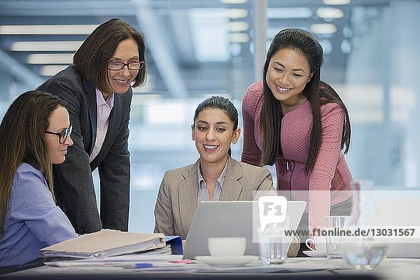 Smiling businesswomen using laptop in conference room meeting