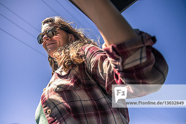 Junge Frau mit Sonnenbrille vor blauem Himmel  Blick aus niedrigem Winkel