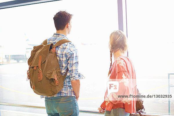 Junges Paar am Flughafen  Rucksäcke tragend  aus dem Fenster schauend